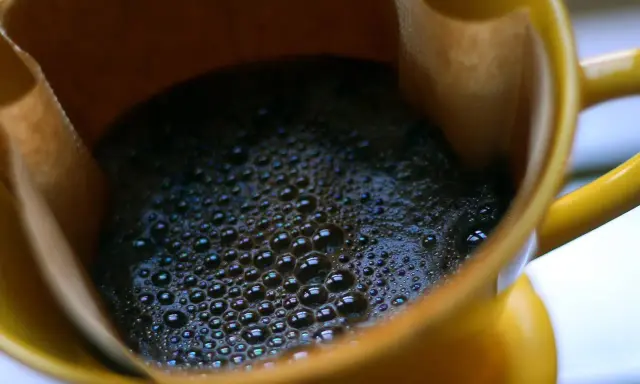 Heißer Kaffee mit Schaum in einer gelben Tasse. Ein Muntermacher, der den Unterschied zwischen Teein und Koffein verdeutlicht.