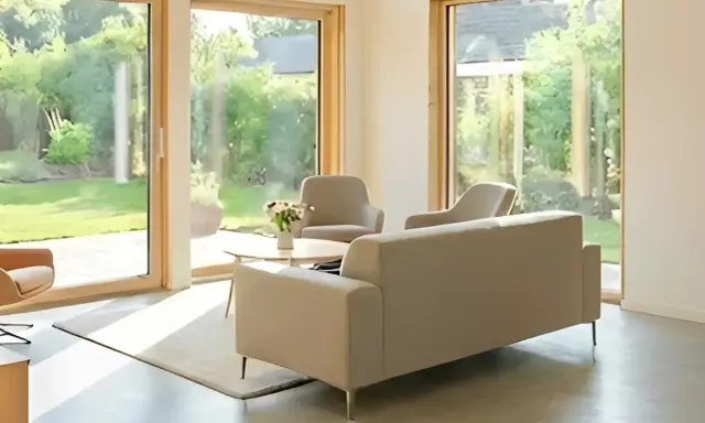 Salón moderno con grandes ventanales que dan a un jardín. Muebles claros y minimalistas. Ideal para aprovechar la luz natural y las deducciones IRPF por eficiencia energética.