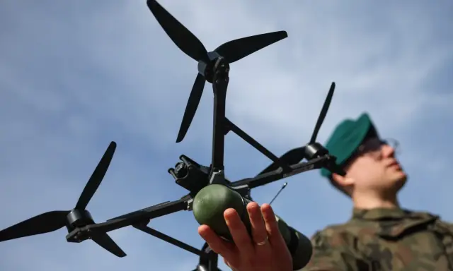 Młody dron wiek. Żołnierz w zielonym beretcie trzyma w dłoniach nowoczesny dron z kamerą i zielonym ładunkiem.