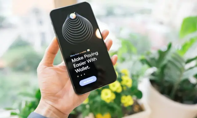 Dłoń trzyma iPhone'a z aplikacją Wallet, która ułatwia płatności dzięki technologii NFC.