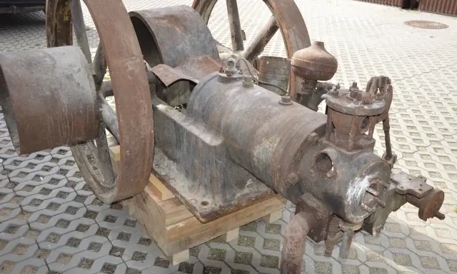 Zardzewiały silnik na gaz drzewny, z dużymi kołami, stoi na drewnianych klockach.