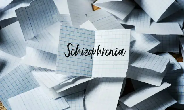 Rozrzucone kartki w kratkę, na jednej napis "Schizophrenia". Obraz symbolizuje chaos myśli, objawy schizofrenii hebefrenicznej.