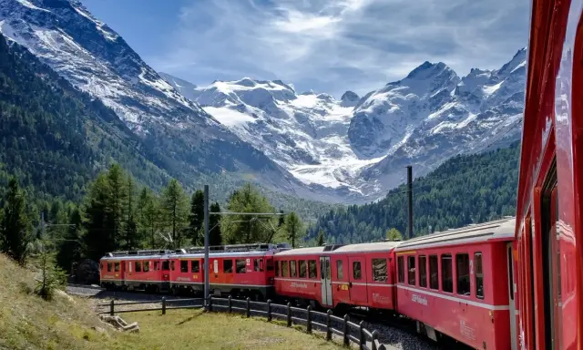 Treni panoramici rossi attraversano un paesaggio alpino mozzafiato con montagne innevate e foreste verdi.