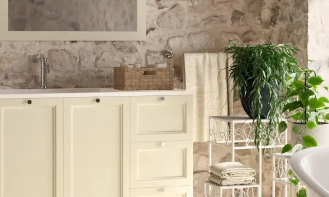 Bagni rustici di campagna con mobile lavabo color crema, cesto in vimini, piante verdi e pareti in pietra grezza.