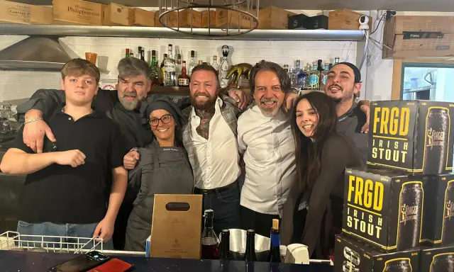 Staff sorridente a Misano Adriatico, con un ragazzo che sembra un gambero sbronzo tra loro. Sul bancone, bottiglie e lattine di "FRGD Irish Stout".