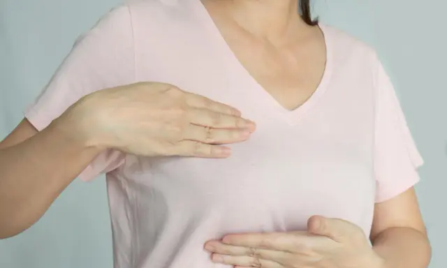 Kobieta bada swoje piersi, doświadczając bólu w piersiach, który może być związany z menopauzą.