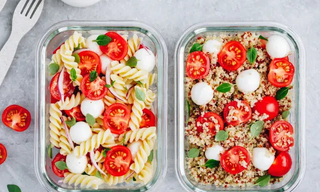 Zwei Glasbehälter mit frischen Mahlzeiten: links Nudelsalat, rechts ein bunter Quinoa-Salat mit Tomaten und Mozzarella.