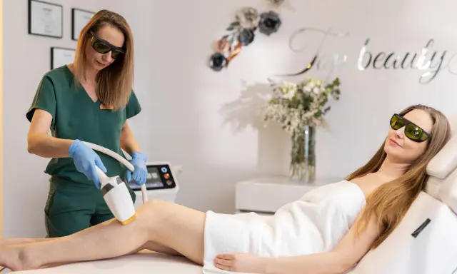 Specjalistka wykonuje zabieg depilacji laserowej, sprawdzając przeciwwskazania fizykoterapii. Klientka leży na kozetce, obie w okularach ochronnych.