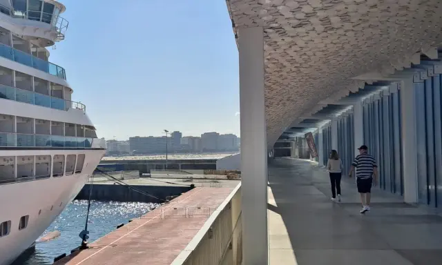 Una nave da crociera attracca nel porto di Leixões, Portogallo. Due persone passeggiano sotto una moderna tettoia con un soffitto decorato.