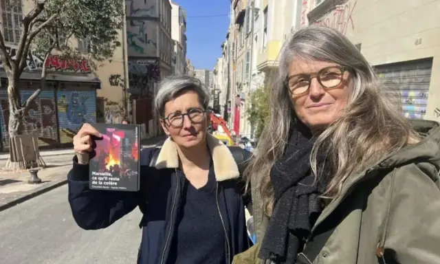 Deux femmes, l'une tenant un livre, dans une rue de Marseille. Le visage de madone de l'une d'elles est encadré par des lunettes.