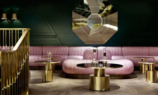 Salon chic avec canapé rose poudré, tables basses dorées et miroir géométrique. Une ambiance **déco belle époque** moderne.