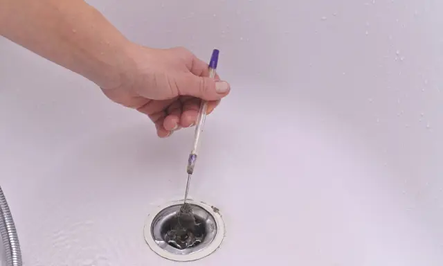 Mano retirando pelos y suciedad del desague plano de una bañera con un bolígrafo.