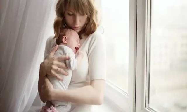 Zmęczona mama tuli płaczące dziecko, które właśnie robi kupę w nocy.