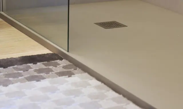 Plato de ducha de resina con desagüe cuadrado. Alfombra a cuadros en primer plano.