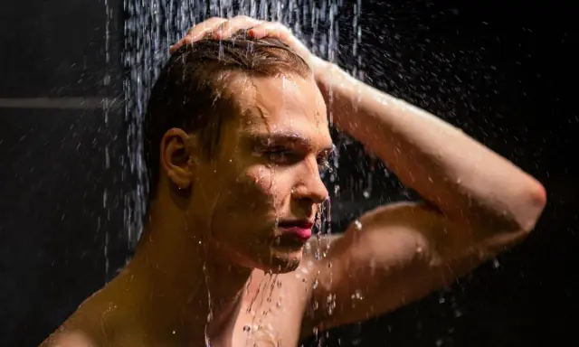 Ein Mann unter der Dusche, der sich die Haare wäscht. Die kalte Dusche ist eine Herausforderung, aber er hält durch.