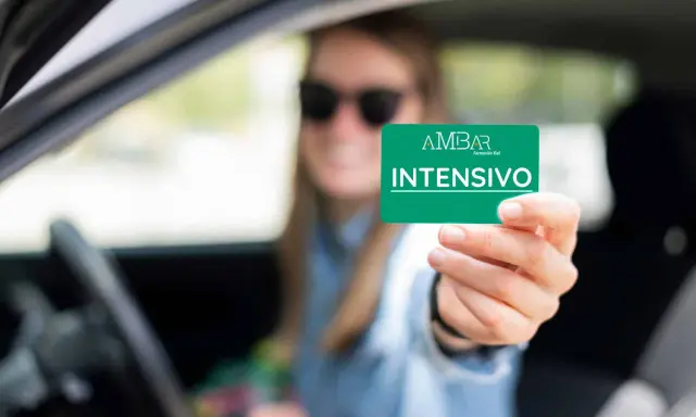 Mujer con gafas de sol muestra tarjeta "INTENSIVO" de autoescuela. Obtener el carnet B+E es difícil, pero este curso intensivo puede ayudar.
