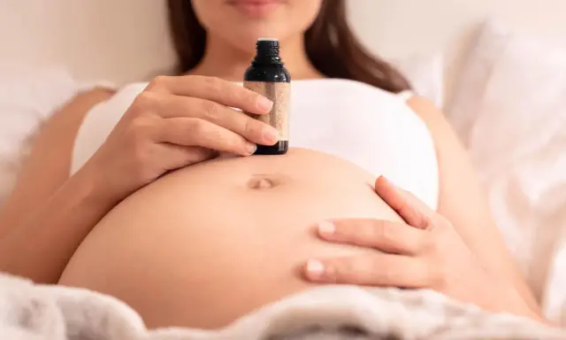 Schwangerenbauch mit einer Hand, die eine kleine Flasche Öl hält. Ab wann Dammmassage?