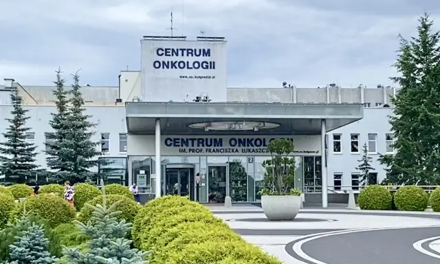 Budynek Centrum Onkologii w Bydgoszczy z zielenią przed wejściem.