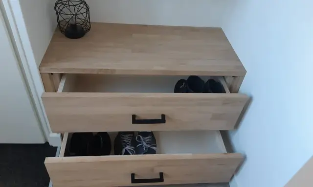 Meuble à chaussures fait maison en bois clair, avec deux tiroirs ouverts contenant des bottes et des baskets.