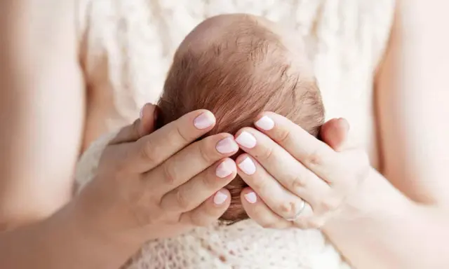 Mani delicate che accarezzano la testa di un neonato, proteggendo la sua fontanella.