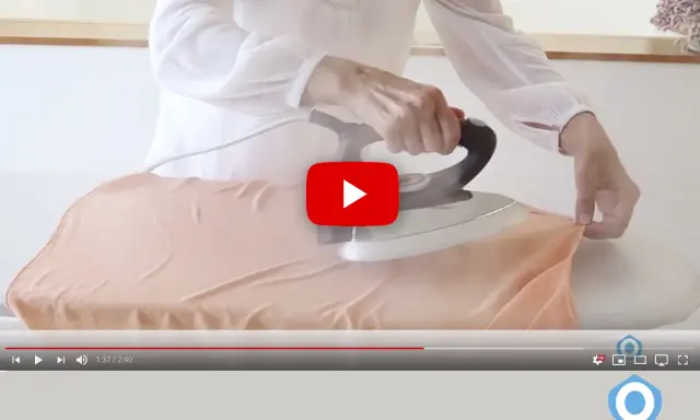 Manos planchando tela de viscosa con vapor en una tabla de planchar.