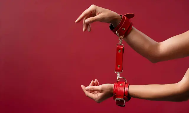 Czerwone kajdanki, symbol bdsm skrót, na nadgarstkach. Dłonie wyciągnięte w geście.