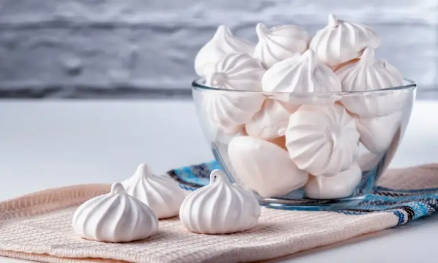 Douceur aérienne : des meringues délicates, comme préparées au bain-marie, dans un bol en verre et sur un tissu texturé.