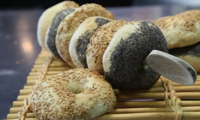 Une rangée de bagels faits maison, certains recouverts de graines de sésame, d'autres de pavot, sur une natte en bambou.