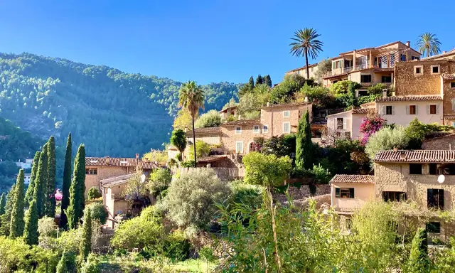Malerische Häuser mit Zypressen und Palmen, ein grüner Berghang im Hintergrund. Ein friedlicher Anblick von Mallorca im Dezember.