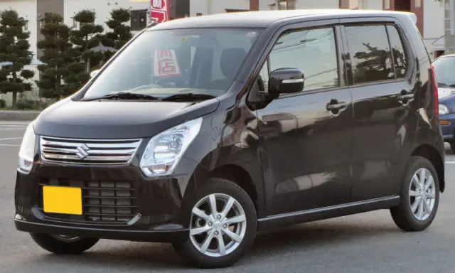 Ciemny Suzuki Wagon R+ z żółtą tablicą rejestracyjną, zaparkowany na ulicy.