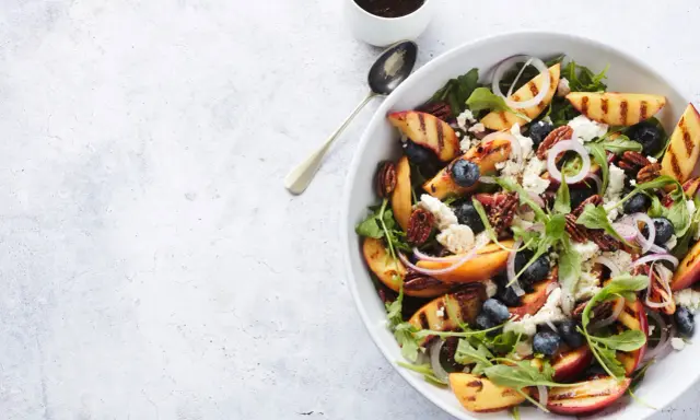 Salat mit Nektarinen, Blaubeeren, Ziegenkäse und Pekannüssen, garniert mit roten Zwiebelringen.