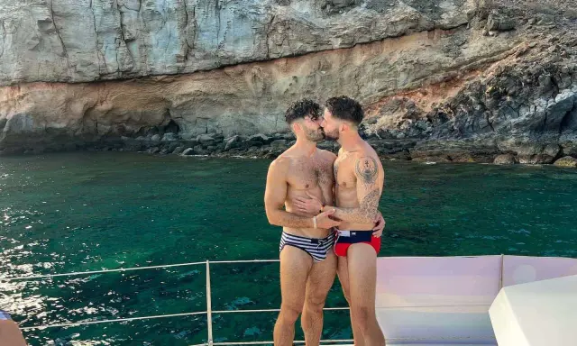 A loving gay couple shares a kiss on a boat, enjoying the stunning scenery of the Canary Islands.