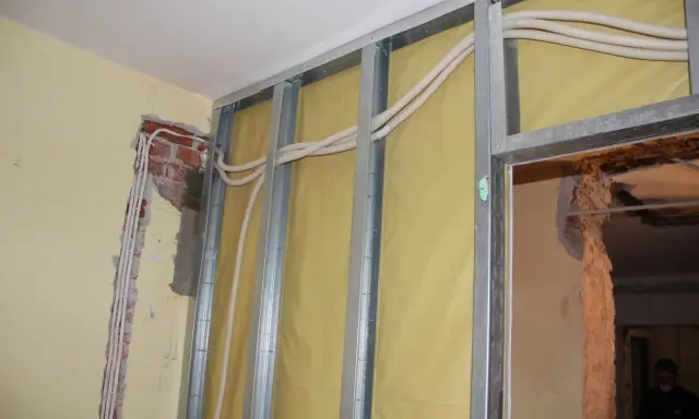 Trwa wymiana instalacji elektrycznej w mieszkaniu. Widać metalowy stelaż, żółtą membranę i nowe przewody elektryczne w peszlach.