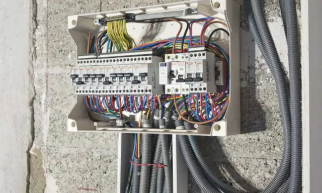 Tableau électrique ouvert, montrant des disjoncteurs de différents calibre et un faisceau de fils colorés.