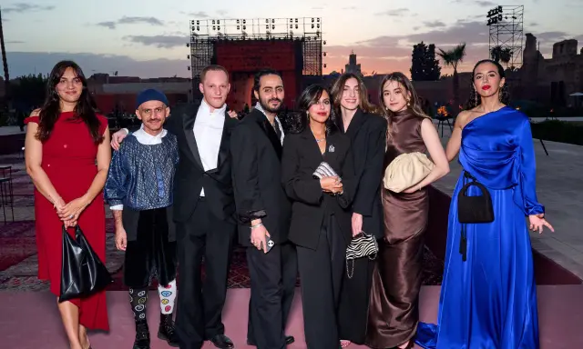 A group poses at a fashion event in Arabia. The backdrop features a large screen with "FASHION TRUST ARABIA" visible.
