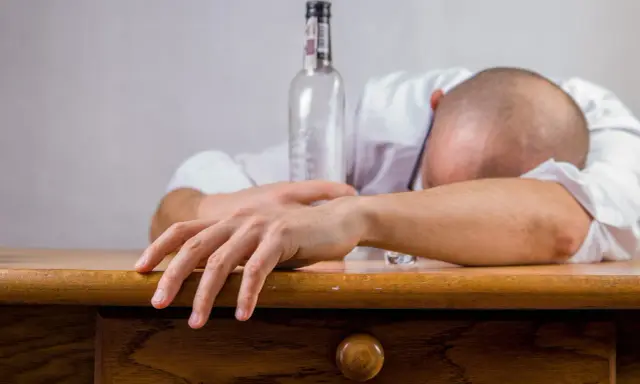Mężczyzna śpi na stole obok pustej butelki. Zastanawiasz się, co wypić przed alkoholem, by uniknąć takiego losu?