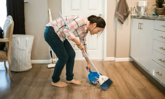 Mujer barriendo el suelo con escoba y recogedor, aplicando trucos de limpieza para mantener el hogar impecable.