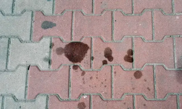 Stare plamy z oleju na kostce brukowej tworzą ciemne ślady, świadczące o dawnych wyciekach.