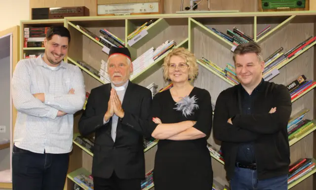 Jacek Ostrowski z książkami w kolejności. Grupa osób pozuje na tle regałów z książkami.