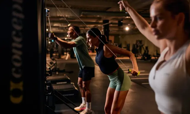 Drei Personen machen ein intensives AMRAP Workout an Kabelzügen. Sie ziehen die Griffe nach hinten und trainieren so ihren Rücken.