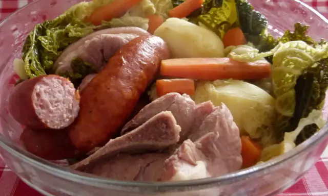 Un plat typique auvergnat : saucisses, porc, pommes de terre, carottes et chou savoyard mijotés dans un grand bol en verre.