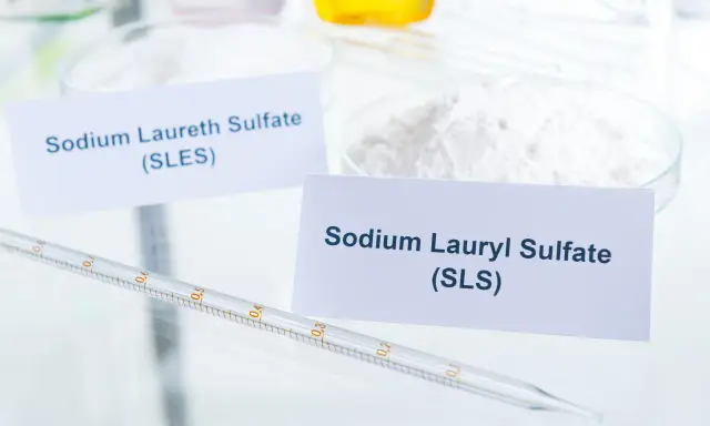 Białe proszki w naczyniach laboratoryjnych, jeden z etykietą "Sodium Laureth Sulfate (SLES)", obok pipeta.