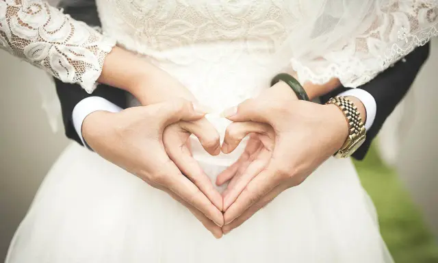 Manos formando un corazón, celebrando 2 años de casados. Vestido de novia blanco y traje negro.