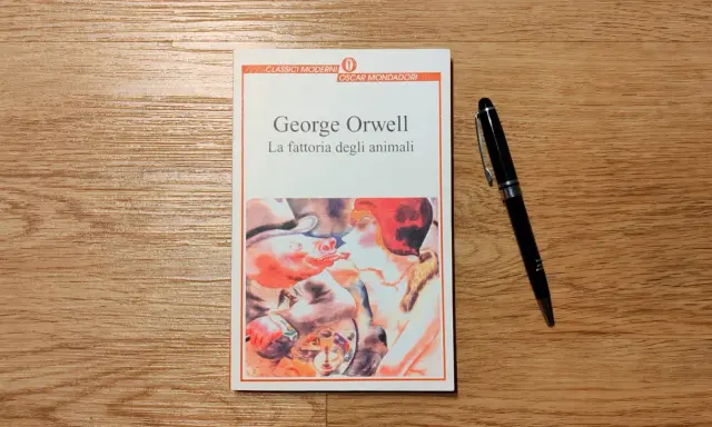 Copertina del libro "La fattoria degli animali" di George Orwell, con una penna nera appoggiata accanto.
