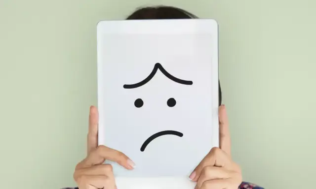 Una persona nasconde il volto dietro un tablet con un'espressione triste disegnata. La famiglia invischiata Minuchin potrebbe sentirsi così.