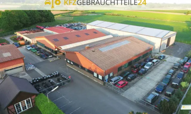 Luftaufnahme eines Autoteile-Lagers mit Gebäuden und vielen Autos.