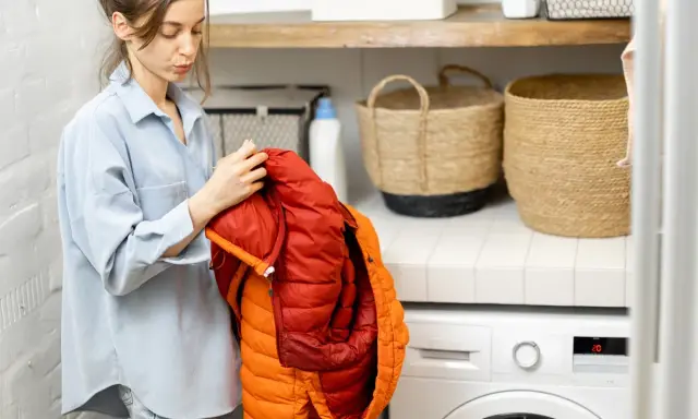 Mujer revisa un anorak naranja y rojo, preparándose para saber como lavar un anorak en la lavadora.