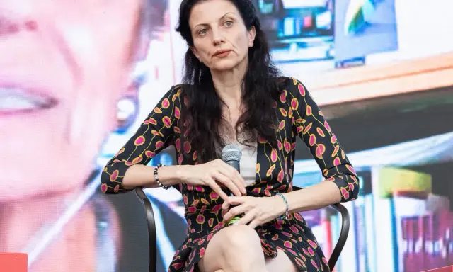 Veronica Tomassini, la cui età non è specificata, con un microfono in mano, indossa una giacca con fantasia floreale.