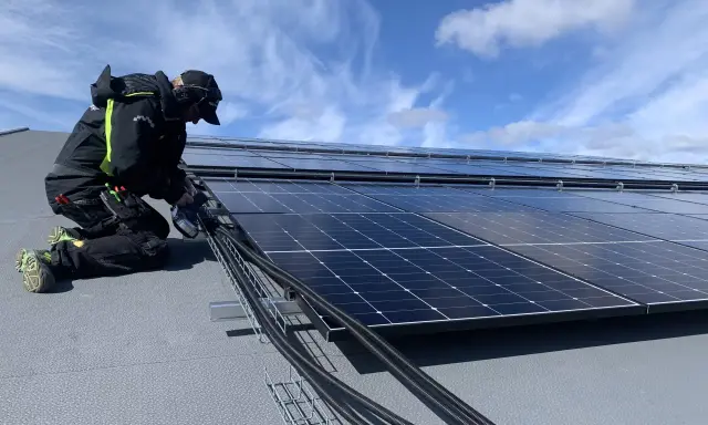 Installatör arbetar med solpaneler, drar kablar. Olika batteri storlekar kan behövas för att optimera energilagringen.