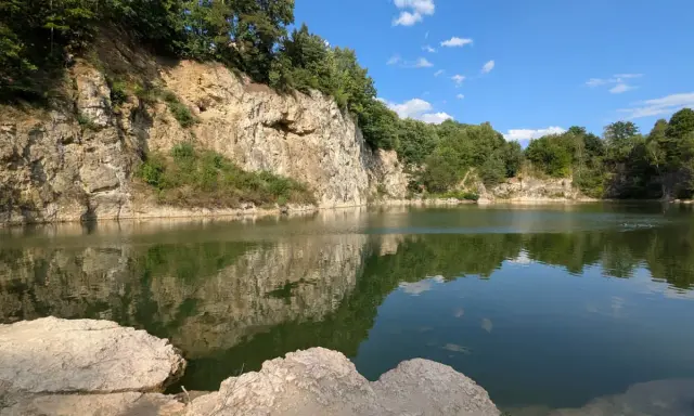 Spokojny zalew kamieniołom w Zabierzowie, z odbijającymi się w wodzie skalnymi ścianami i zielenią drzew.